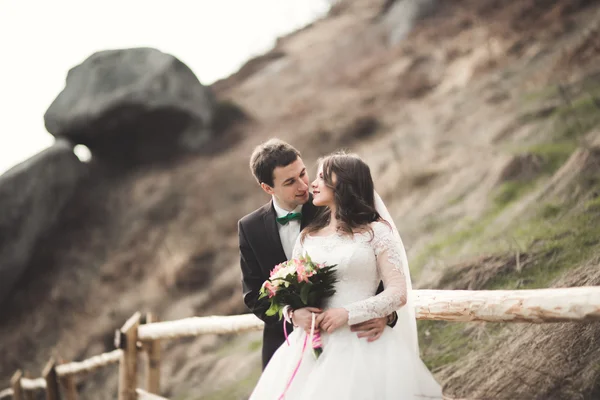 Щаслива весільна пара цілується і обіймається біля високої скелі — стокове фото