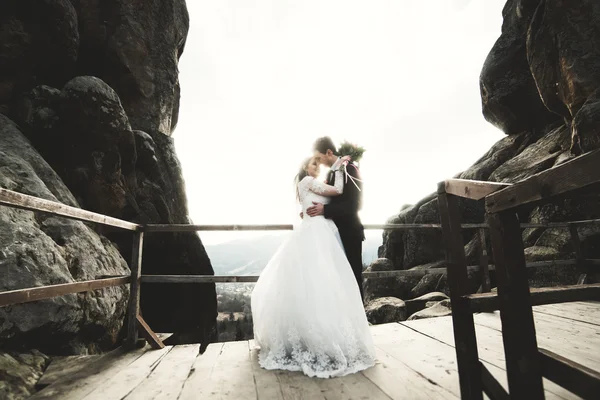Bruiloft koppel in liefde kussen en knuffelen in de buurt van rotsen op prachtig landschap — Stockfoto