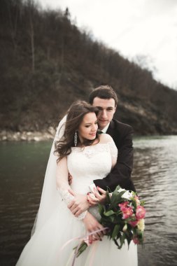 Öpüşme ve taşlarla Nehri yakınında kucaklayan güzel düğün çifti