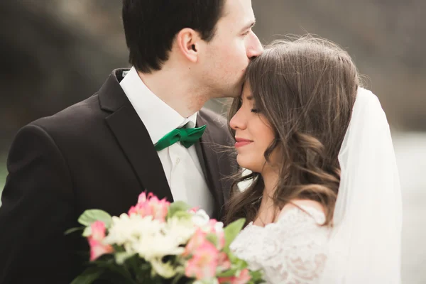 Felice coppia di nozze, sposa e sposo posa fiume pulito sullo sfondo delle montagne — Foto Stock