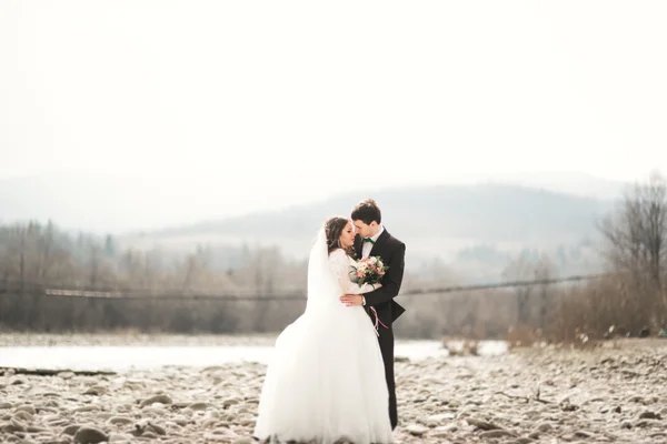 Felice coppia di nozze, sposa e sposo posa fiume pulito sullo sfondo delle montagne — Foto Stock