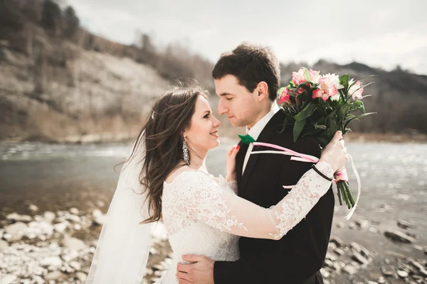 Casal de casamento feliz, noiva e noivo posando rio puro contra o pano de fundo das montanhas — Fotografia de Stock