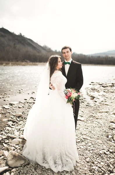 Gyönyörű esküvői pár csók, és átfogó, kövekkel-folyó közelében — Stock Fotó