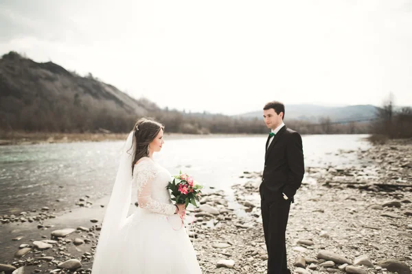 Hermosa pareja de boda besándose y abrazándose cerca del río con piedras —  Fotos de Stock