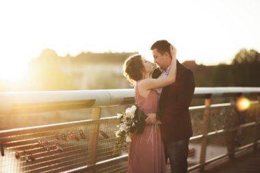 Şık Düğün çifti, damat, Gelin öpüşme ve günbatımında bir köprüde sarılma pembe elbise ile sevgi dolu