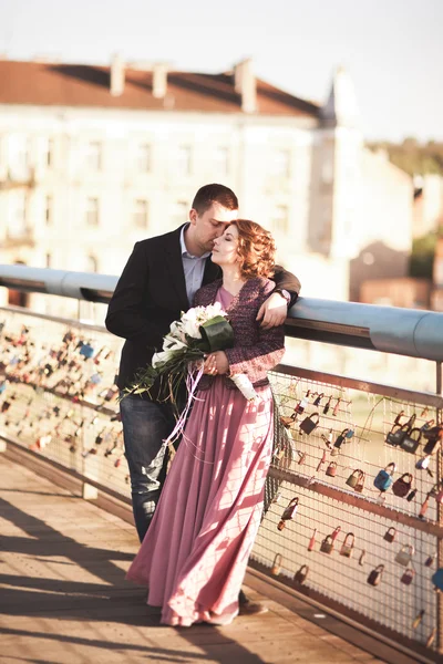 Şık Düğün çifti, damat, Gelin öpüşme ve günbatımında bir köprüde sarılma pembe elbise ile sevgi dolu — Stok fotoğraf