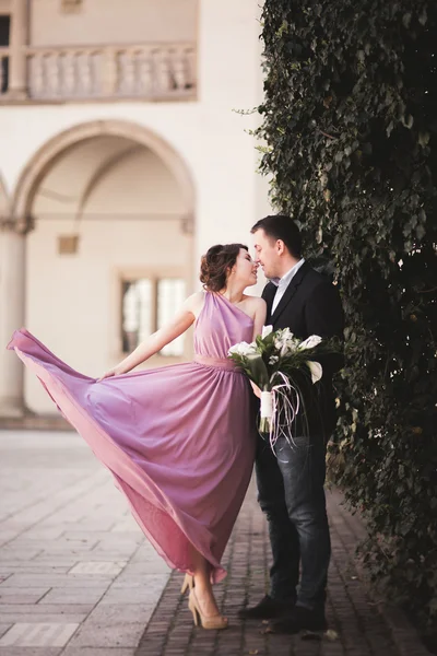 Šťastný, Svatební pár, ženich, nevěsta s růžové šaty objímání a usmívá se vzájemně na pozadí stěny v zámku — Stock fotografie