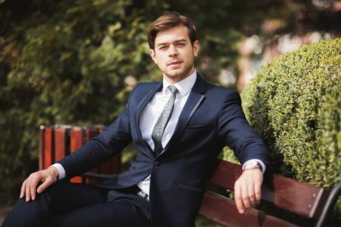 Yakışıklı, şık, genç bir iş adamı. Açık havada portre pozu veriyor.