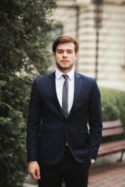 Yakışıklı, şık, genç bir iş adamı. Açık havada portre pozu veriyor.