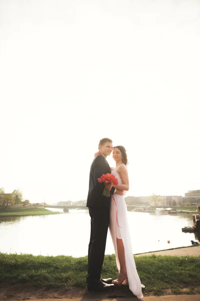 Élégant beau couple de mariage posant près de la rivière au coucher du soleil — Photo