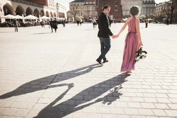 Wedding. beautiful couple, bride with pink dress walking in the old city Krakow, their shadows — Stock Photo, Image