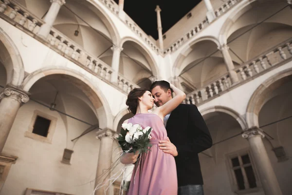 Šťastný, Svatební pár, ženich, nevěsta s růžové šaty objímání a usmívá se vzájemně na pozadí stěny v zámku — Stock fotografie