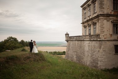Güzel, romantik bir düğün. Yeni evliler. Eski kalenin yakınlarında sarılıyorlar.