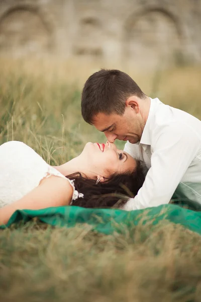 Casal de casamento feliz deitado na grama verde na hora de verão — Fotografia de Stock