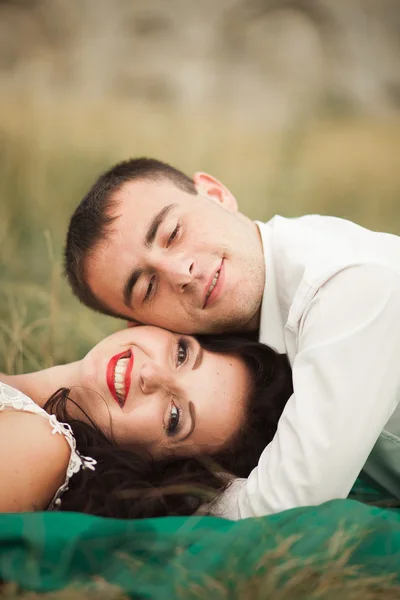 Casal de casamento feliz deitado na grama verde na hora de verão — Fotografia de Stock