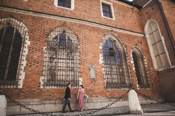 Wspaniały ślub para, pana młodego i panny młodej z różowej sukience chodzenie na starym mieście w Krakowie — Zdjęcie stockowe