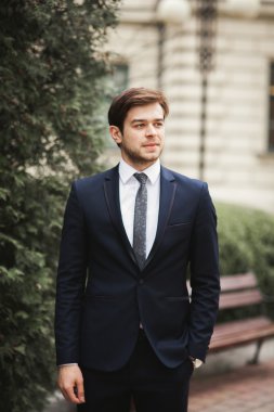 Yakışıklı, şık, genç bir iş adamı. Açık havada portre pozu veriyor.