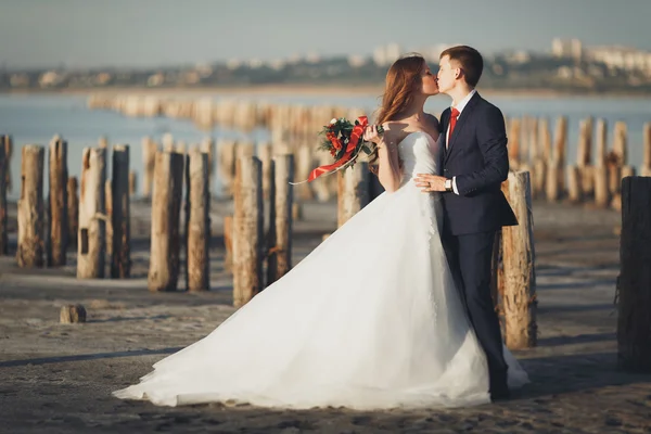 Mariage couple, marié, mariée avec bouquet posant près de la mer au coucher du soleil — Photo