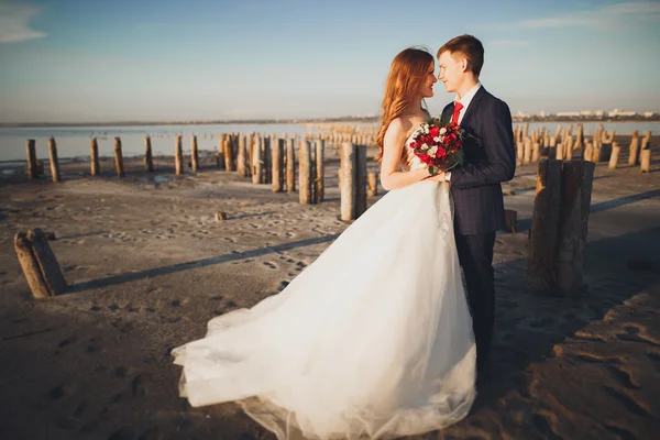 Beau jeune couple de mariage, mariée et marié posant près des poteaux en bois sur la mer de fond — Photo