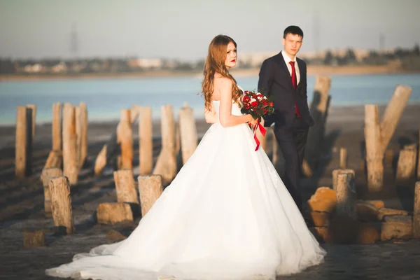 Piękny ślub młodej pary, Narzeczeni pozowanie w pobliżu drewnianych słupów na tle morza — Zdjęcie stockowe