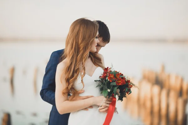 Pareja de boda, novio, novia con ramo posando cerca del mar al atardecer — Foto de Stock