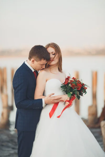 Beautiful young wedding couple, bride and groom posing near wooden poles on the background sea — Stock Photo, Image