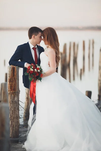 Esküvő házaspár, vőlegény, menyasszony a csokrot pózol a tenger a sunset — Stock Fotó