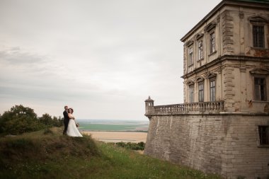 Güzel, romantik bir düğün. Yeni evliler. Eski kalenin yakınlarında sarılıyorlar.