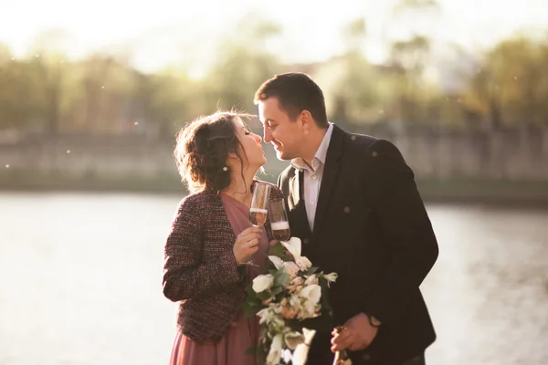 Couple de mariage, marié et robe posant près de la rivière avec un verre au coucher du soleil — Photo