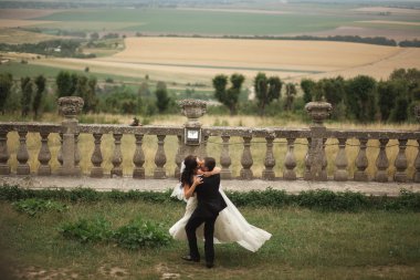 Güzel, romantik bir düğün. Yeni evliler. Eski kalenin yakınlarında sarılıyorlar.