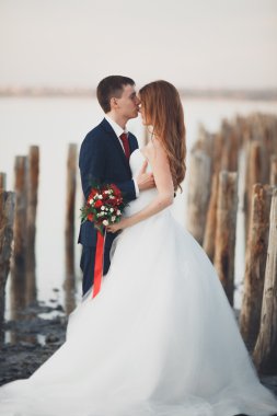 Çift düğün, damat, gelin buketi günbatımı üzerinde denize yakın poz ile