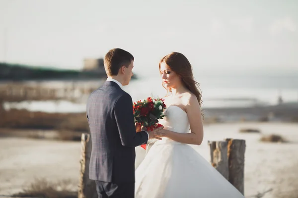 Matrimonio coppia, sposo, sposa con bouquet posa vicino al mare al tramonto — Foto Stock