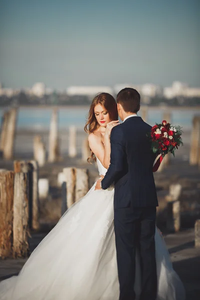 Pareja de boda, novio, novia con ramo posando cerca del mar al atardecer — Foto de Stock