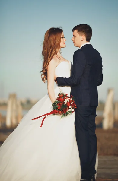 Beautiful young wedding couple, bride and groom posing near wooden poles on the background sea — Stock Photo, Image