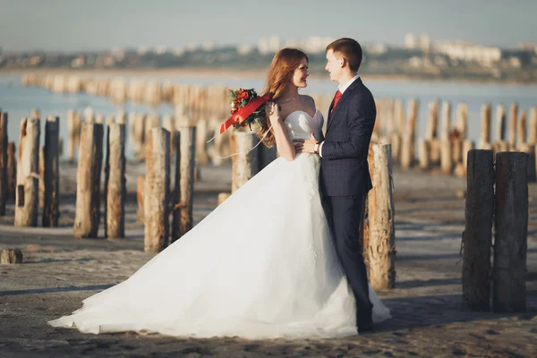 Mariage couple, marié, mariée avec bouquet posant près de la mer au coucher du soleil — Photo