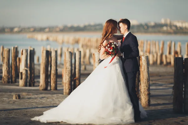 Свадебная пара, жених, невеста с букетом, позирующим у моря на закате — стоковое фото