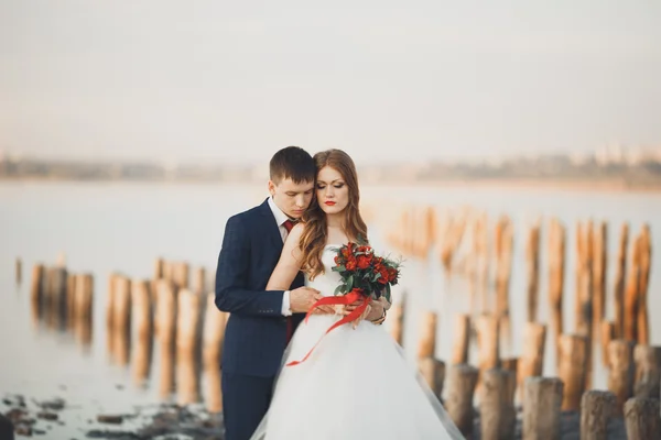 Matrimonio coppia, sposo, sposa con bouquet posa vicino al mare al tramonto — Foto Stock