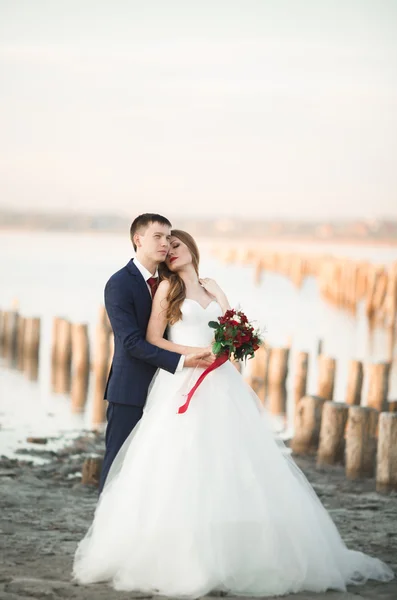 Pareja de boda, novio, novia con ramo posando cerca del mar al atardecer —  Fotos de Stock