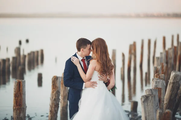 Beau jeune couple de mariage, mariée et marié posant près des poteaux en bois sur la mer de fond — Photo