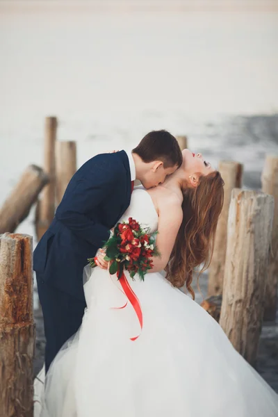 Beau jeune couple de mariage, mariée et marié posant près des poteaux en bois sur la mer de fond — Photo