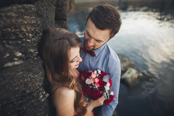 Pareja de boda sentada en piedra grande alrededor del mar azul — Foto de Stock