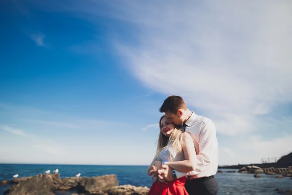 Romantické milující pár pózuje na kamenech nedaleko moře, modrá obloha — Stock fotografie