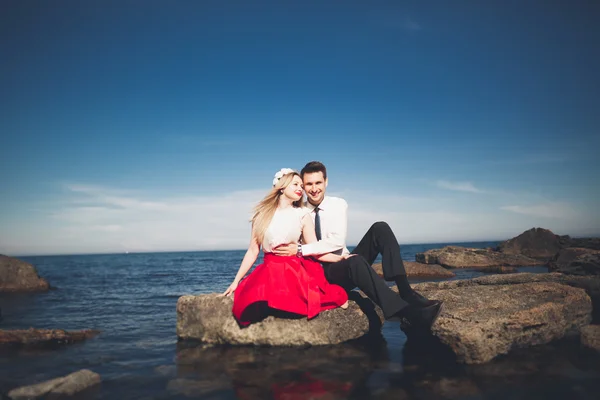 Ρομαντικό ζευγάρι ερωτευμένων που παρουσιάζουν στις πέτρες κοντά στη θάλασσα, μπλε ουρανό — Φωτογραφία Αρχείου