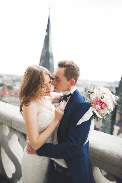 Pasangan pengantin yang cantik bergaya berciuman dan berpelukan di latar belakang panorama kota tua — Stok Foto