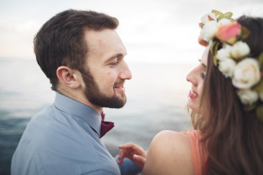 Düğün çifti mavi denizin yanındaki kayalarda öpüşüyor ve sarılıyor.