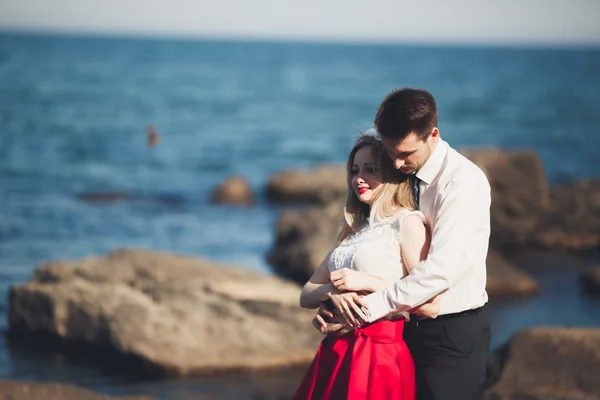 Romantické milující pár pózuje na kamenech nedaleko moře, modrá obloha — Stock fotografie