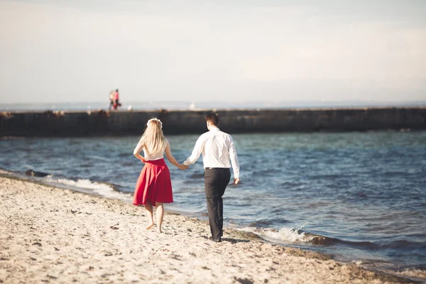 Unga lyckliga par promenader på stranden leende anläggningen runt varandra. Kärlekshistoria — Stockfoto