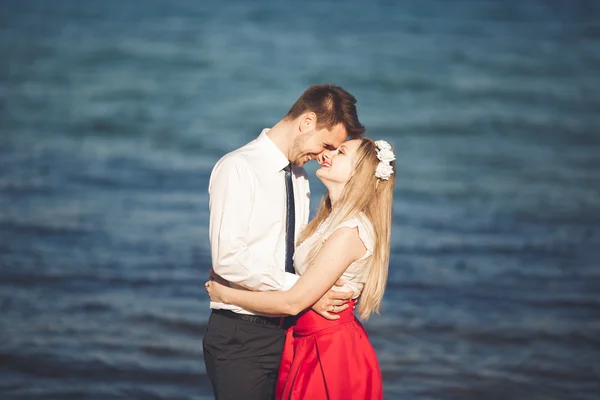 Junges glückliches Paar, das lächelnd am Strand spaziert und sich umschlingt. Liebesgeschichte — Stockfoto