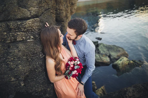 Matrimonio coppia baci e abbracci su rocce vicino al mare blu — Foto Stock