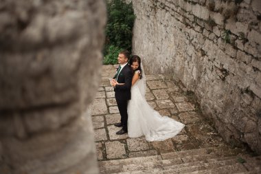 Güzel, romantik bir düğün. Yeni evliler. Eski kalenin yakınlarında sarılıyorlar.